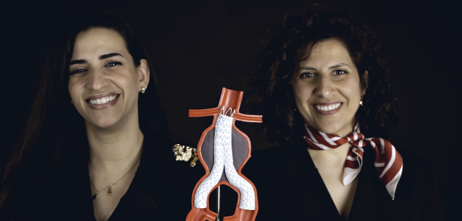 Acunex co-founders Yathreb Asaad-Helou and Areen Shtewe holding an anatomical model of an abdominal aortic aneurysm with a deployed endograft.